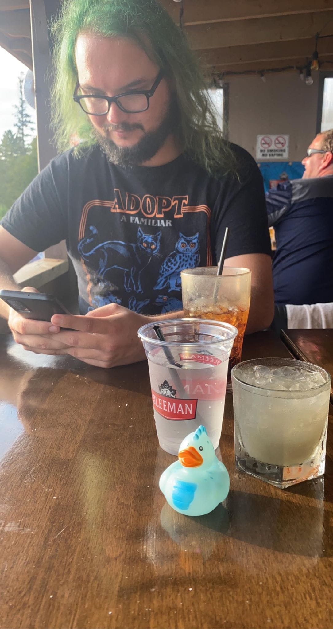 A man with green hair looks at his phone at a resturaunt